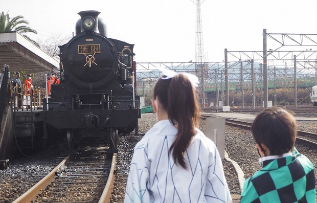 Dua orang anak yang ber-cosplay karakter dari anime Kinmetsu no Yaiba saat berfoto di depan kereta wisata tematik