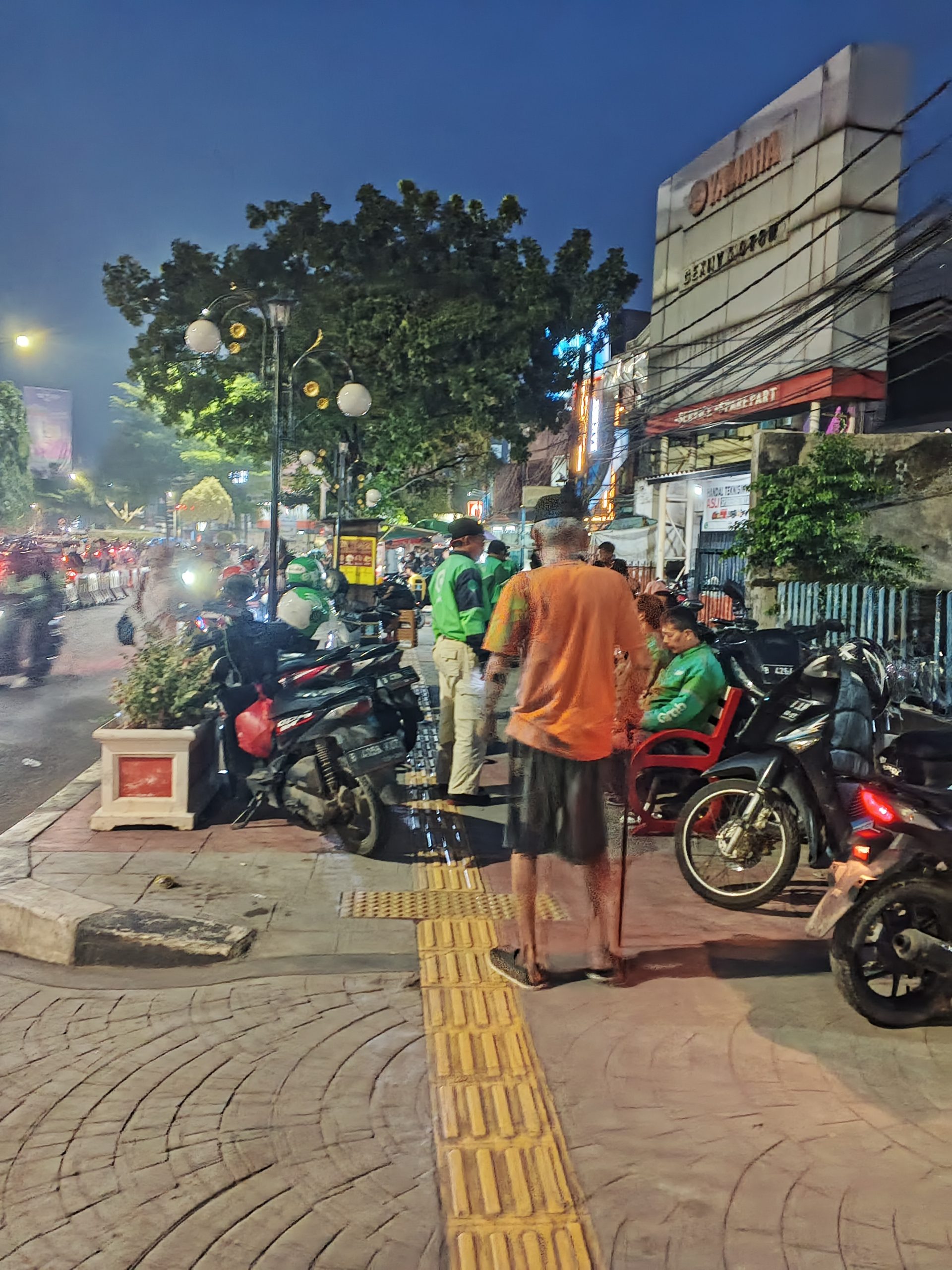 Seorang kakek berjalan kaki tertatih-tatih dengan tongkatnya di trotoar sementara jalannya dihalangi oleh motor-motor yang terparkir dan gerobak Pedagang Kaki Lima (PKL). Bagaimana perasaan anda jika mengetahui bahwa kakek tersebut adalah kakek kesayangan anda? | Foto: RED/Adrian Falah Diratama